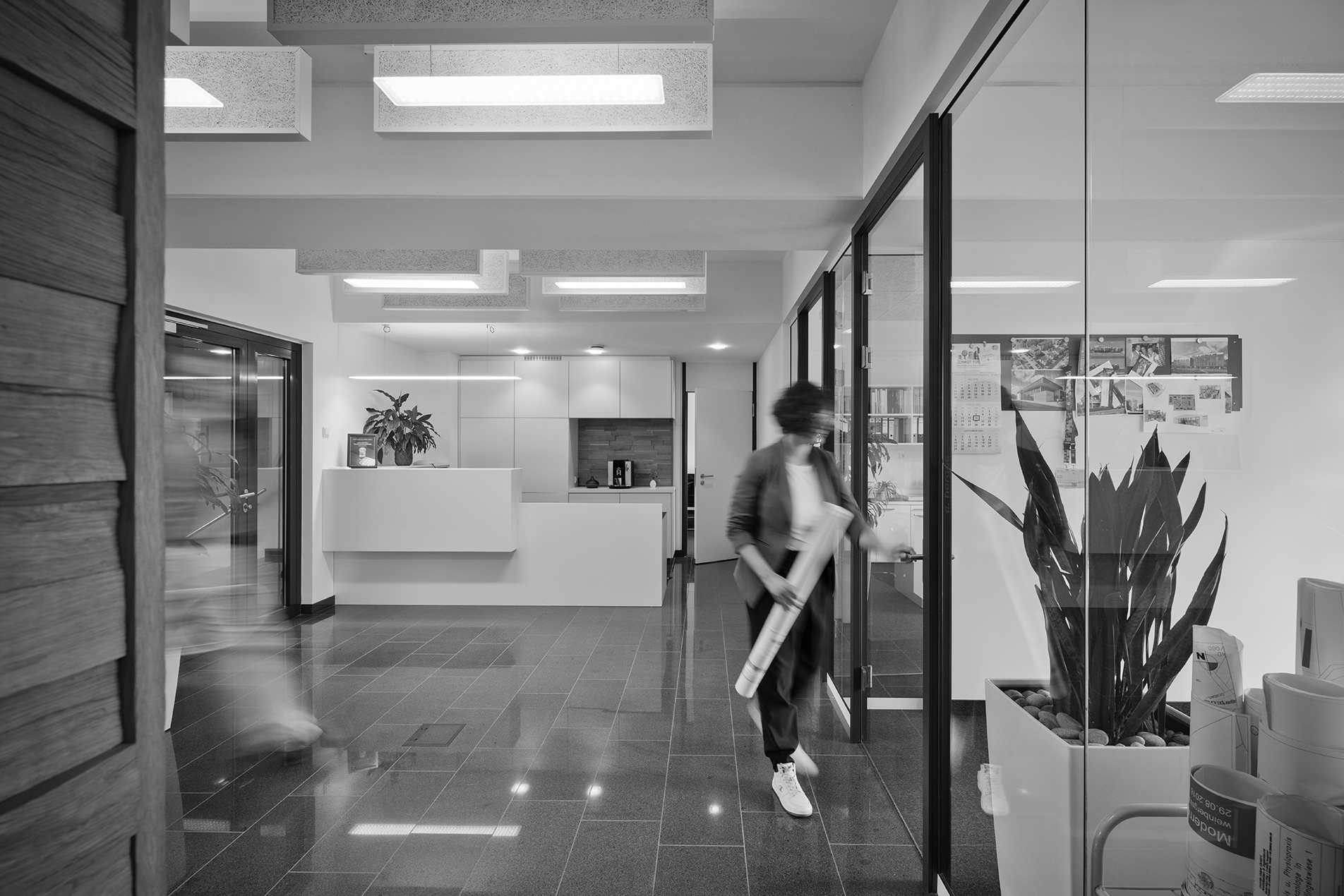 Blick in den Flur des Büros von Haid Architekten | Ingenieure, auf der rechten Seite diverse Einzelbüros mit Glasfronten, gerade aus Empfangstheke, linke Hand Eingangstüre